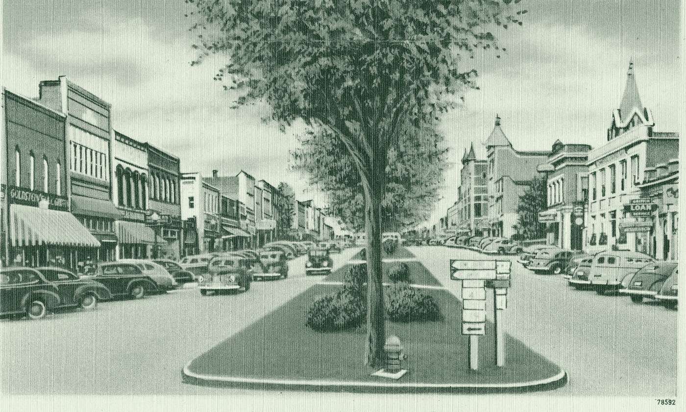 Hill Street in downtown Griffin, from a 1930s–40s postcard: storefronts, a tree-lined median and parked cars
